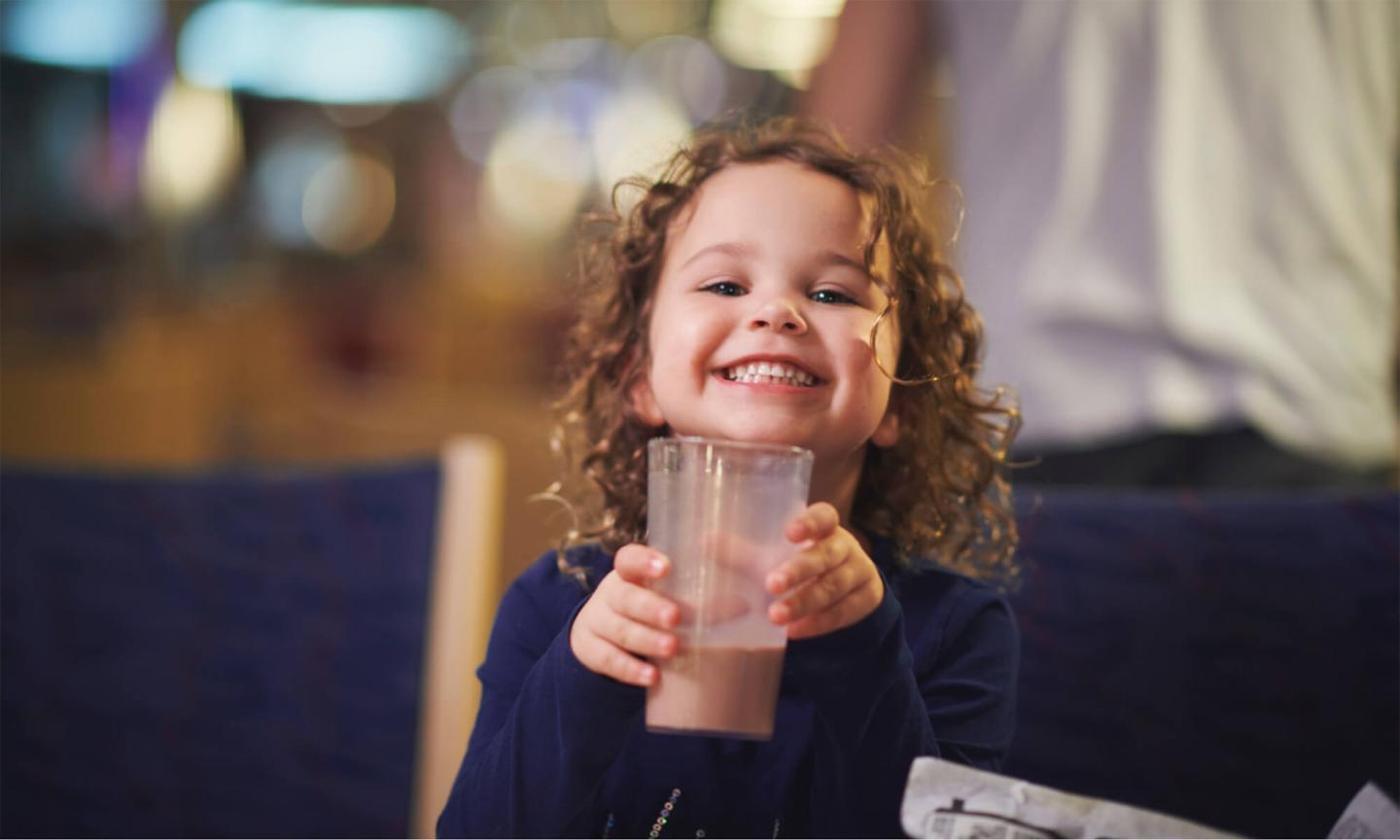A young girl with curly hair smiling while holding a glass of chocolate milk.